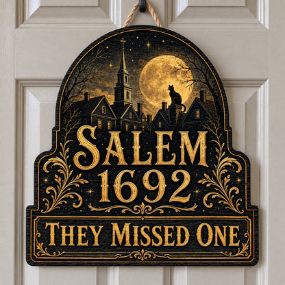 Custom-cut wooden sign reading “SALEM 1692” and “THEY MISSED ONE” with a black cat on a moonlit village and gold filigre