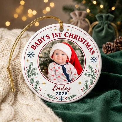 Round ceramic ornament with 'BABY'S 1ST CHRISTMAS', pine sprigs, snowflakes, gold stars, red rings, and a photo frame