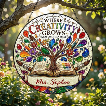Round stained glass-style suncatcher with tree growing from an open book, paintbrushes, pencils, blossoms, and teacher n