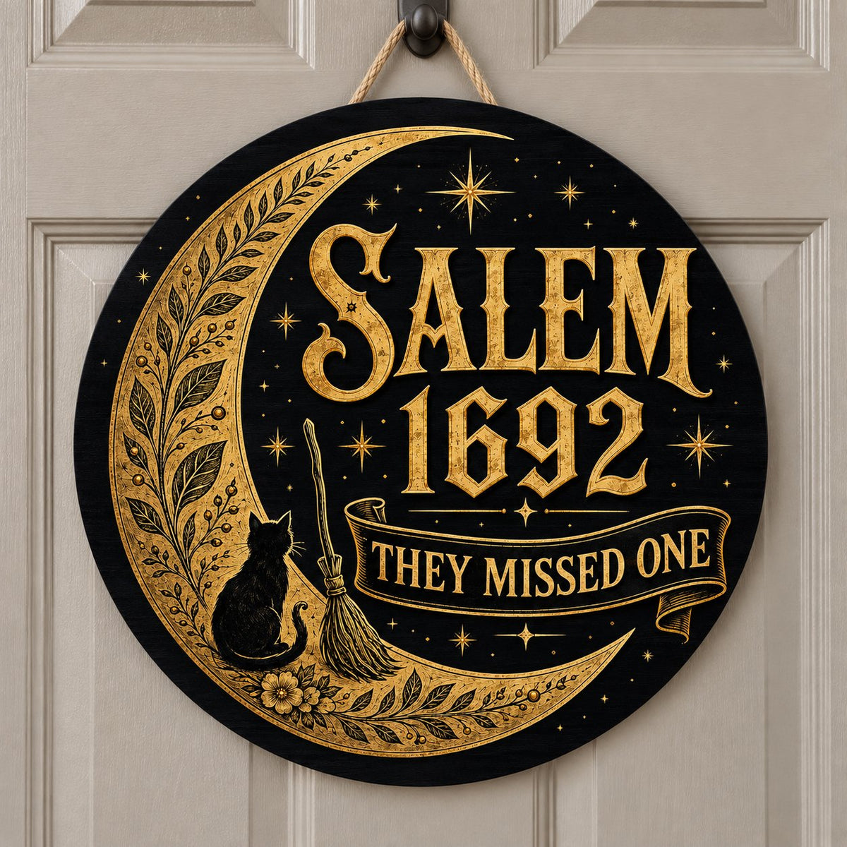 Round wooden sign with gold crescent moon, black cat, broomstick, stars and 'SALEM 1692 THEY MISSED ONE' on black.