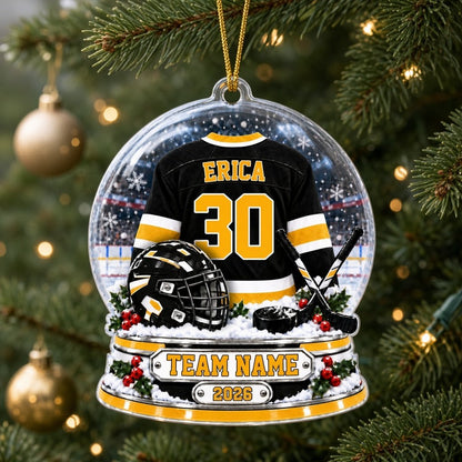 Snow globe acrylic ornament with black and gold hockey jersey, crossed sticks, puck, holly and a year plaque.