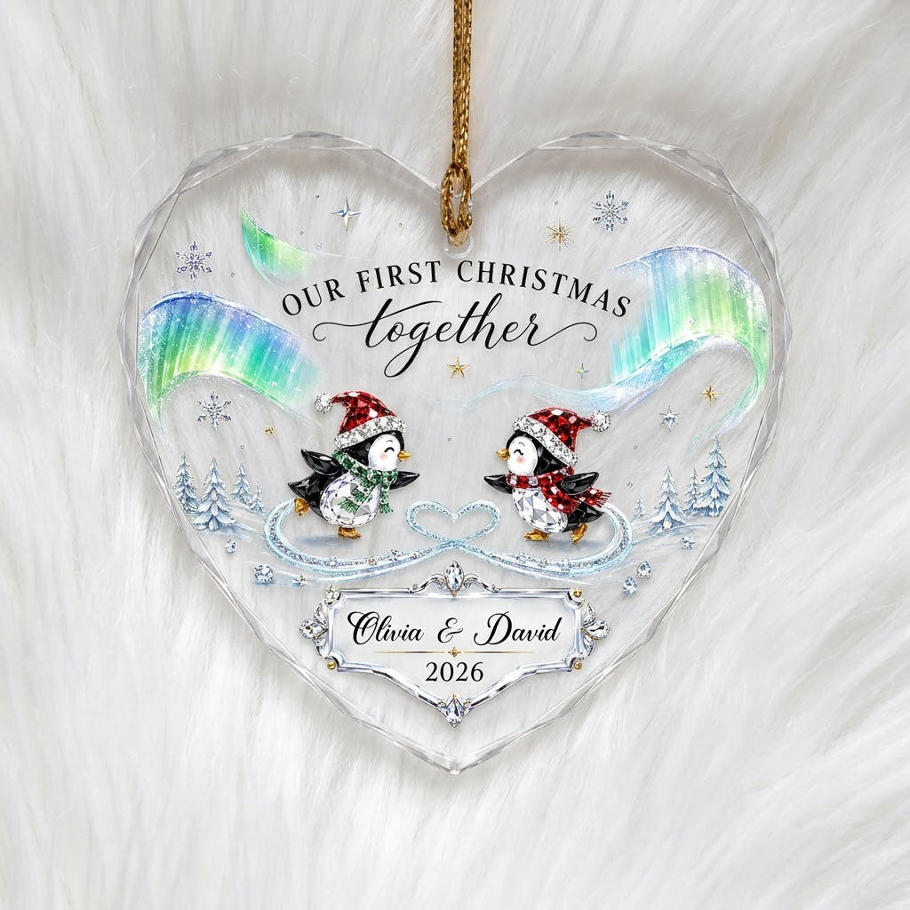 Heart glass ornament with two ice-skating penguins under green and blue aurora with names and date.