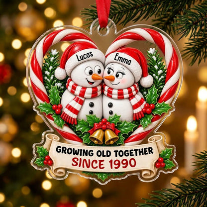 Two snowmen touching noses inside a candy-cane heart with holly, gold bells, and a scroll banner with names and year.