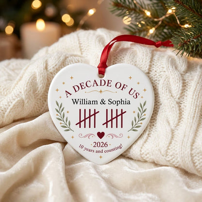 Heart ceramic ornament with 'A Decade of Us', • 2026 •, tally marks, green branches, gold stars, and couple names.