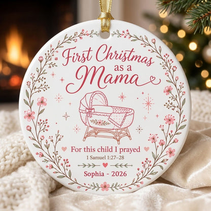Round ceramic ornament with pink floral wreath, baby bassinet line art, stars, and First Christmas as a Mama.