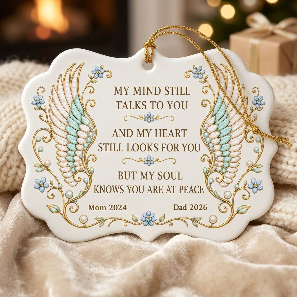Medallion ceramic ornament with gold-outlined angel wings, blue forget-me-nots, and a memorial quote with name and year.