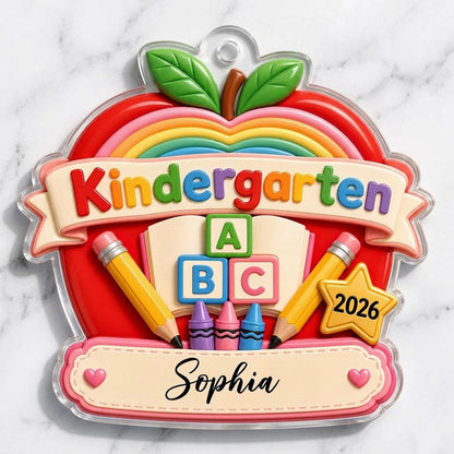 Red apple acrylic ornament with 'Kindergarten 2026', rainbow, ABC blocks, crayons, pencils, star badge, and a name banne