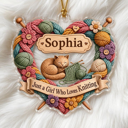 Heart-shaped acrylic ornament with yarn wreath, knitting needles, brown cat and "Just a Girl Who Loves Knitting" text.