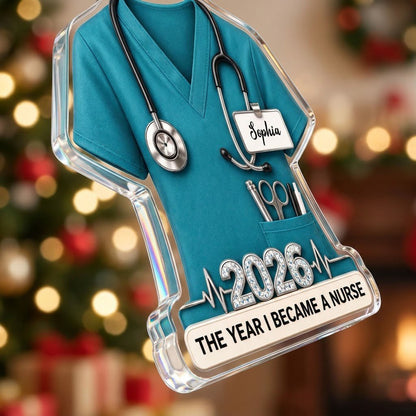 Teal scrub top acrylic ornament with stethoscope, ID badge, pocket tools, EKG line, 2026 numerals and a white name banne