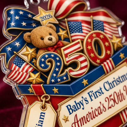 A teddy bear in a red gift box with blue trim, 250 and 2026 with American flags and a patriotic bow on an acrylic orname
