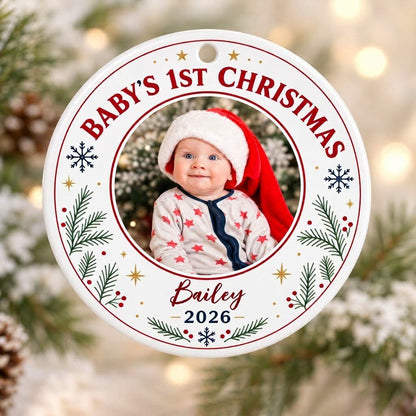 Round ceramic ornament with 'BABY'S 1ST CHRISTMAS', pine sprigs, snowflakes, gold stars, red rings, and a photo frame