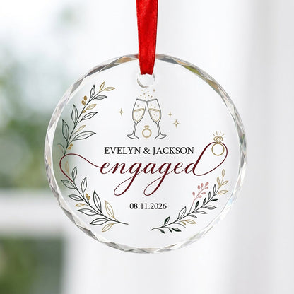 Round glass ornament with clinking champagne flutes, sparkles, ring and botanical foliage with burgundy ribbon and the w
