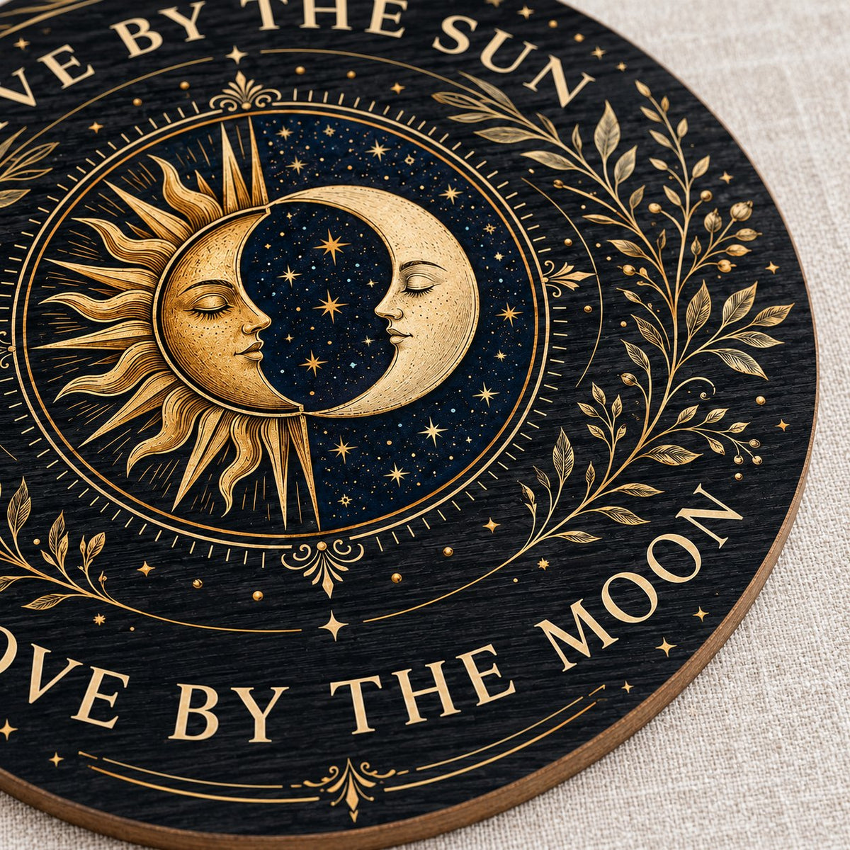 Round wooden sign with gold sun and crescent moon faces and the words “Live By The Sun, Love By The Moon”.