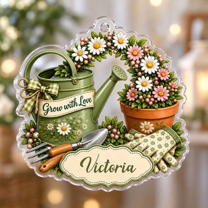Green watering can with bow, garden tools, and floral pot with ‘Grow with Love’ and a name on a clear acrylic ornament.