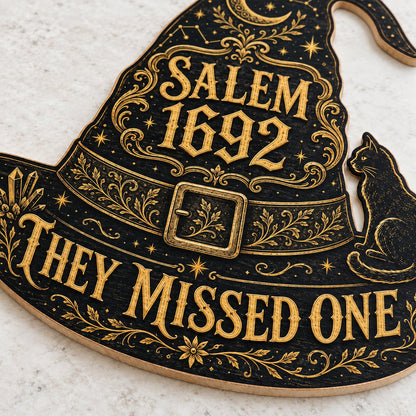 Witch hat-shaped wooden sign with 'SALEM 1692 THEY MISSED ONE', crescent moon, stars, filigree, and a black cat on the b