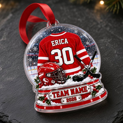Acrylic snow globe ornament with red hockey jersey, helmet, crossed sticks, puck, holly and a silver name plaque.