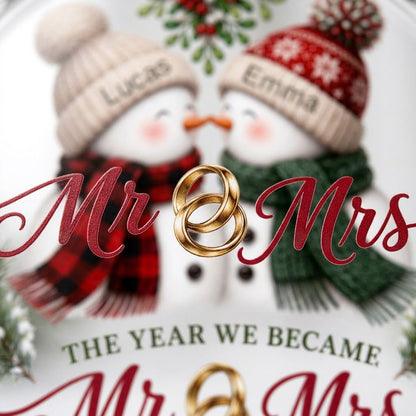 Round faceted glass ornament with two kissing snowmen under mistletoe and gold rings, personalized with names.