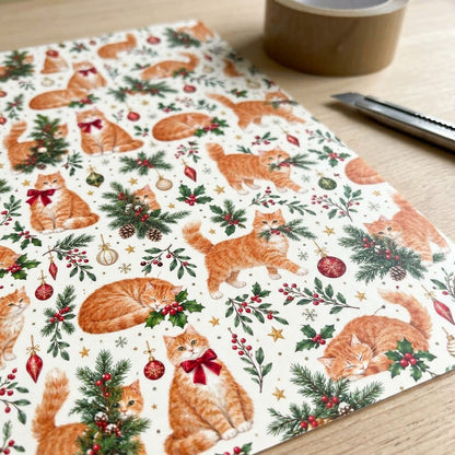 Cream gift wrap with ginger tabby cats, red and gold ornaments, pine boughs, berries and stars in a pattern.