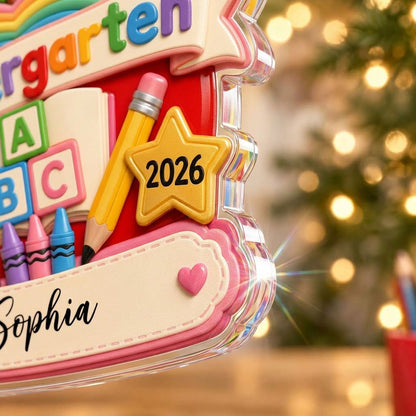 Red apple acrylic ornament with 'Kindergarten 2026', rainbow, ABC blocks, crayons, pencils, star badge, and a name banne