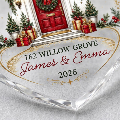 Heart-shaped glass ornament with a red front door, wreath, garland, lanterns, gift boxes, and gold snowflakes.