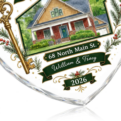Heart-shaped glass ornament with watercolor house, gold key, evergreens, green banners, and 'Our New Home' text.