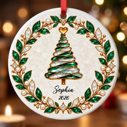 Round ceramic ornament with an emerald jeweled spiral Christmas tree and gold filigree wreath on cream.