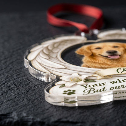 Clear acrylic angel wings ornament with a circular dog photo, white lilies, a dark green paw print, and a name banner.