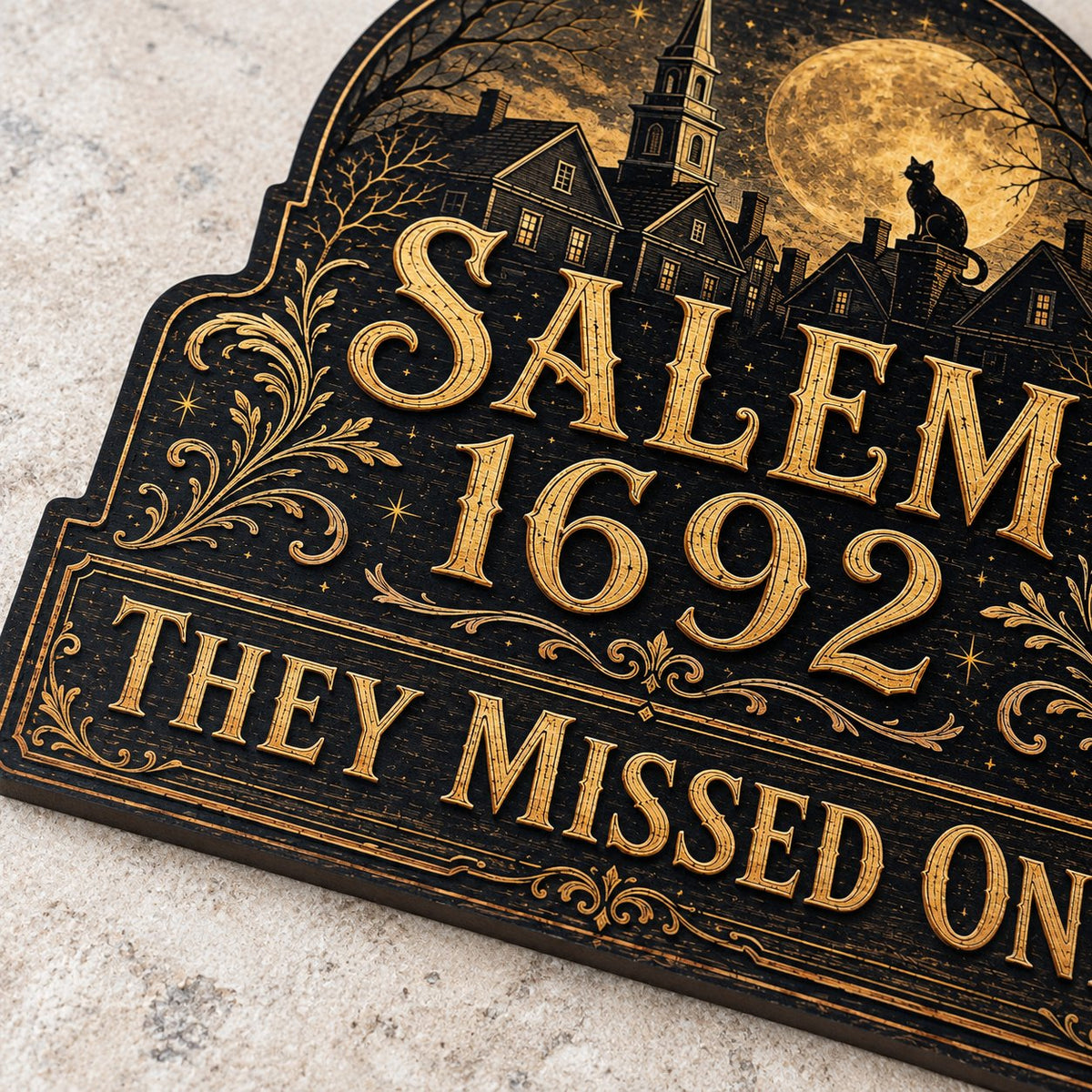 Custom-cut wooden sign reading “SALEM 1692” and “THEY MISSED ONE” with a black cat on a moonlit village and gold filigre