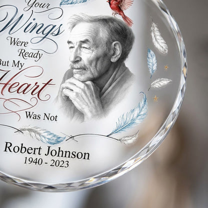 Round glass ornament with sketch portrait, two red cardinals, blue and brown feathers, and memorial name and years.