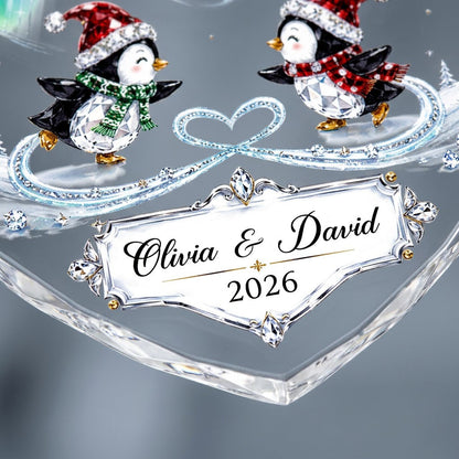 Heart glass ornament with two ice-skating penguins under green and blue aurora with names and date.