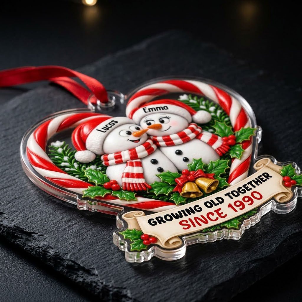 Two snowmen touching noses inside a candy-cane heart with holly, gold bells, and a scroll banner with names and year.