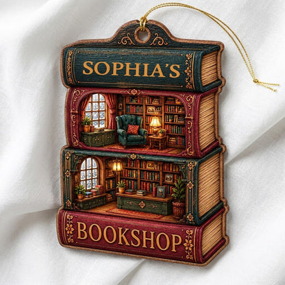 Custom-cut ornament of stacked books showing cozy bookshop rooms, BOOKSHOP text, and a personalized name.