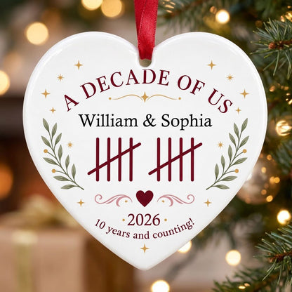 Heart ceramic ornament with 'A Decade of Us', • 2026 •, tally marks, green branches, gold stars, and couple names.