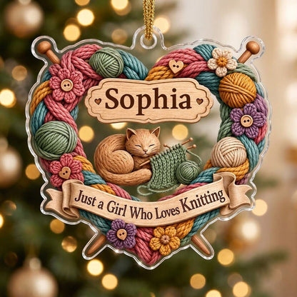 Heart-shaped acrylic ornament with yarn wreath, knitting needles, brown cat and "Just a Girl Who Loves Knitting" text.