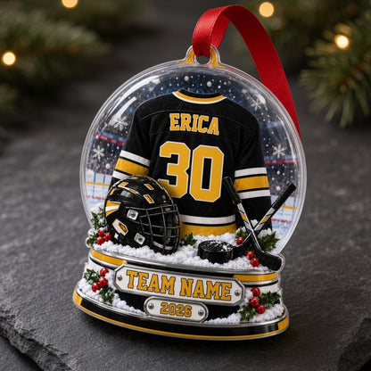Acrylic snow globe ornament with hockey jersey, helmet, crossed sticks, puck, holly, and a silver plaque base.
