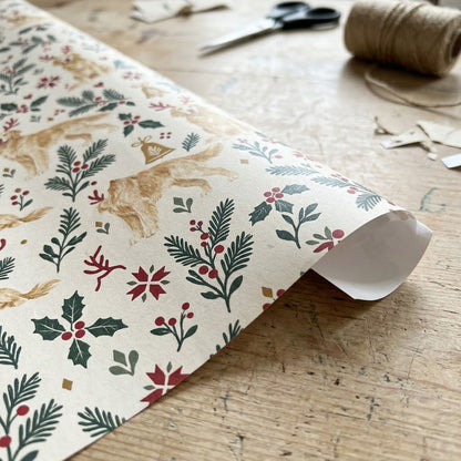 Cream wrapping paper with golden retrievers in red antler headbands, pine sprigs, red berries and gold bells.