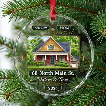 Round glass ornament with watercolor house, green and gold banners, gold key, pine branches, and address and year plaque