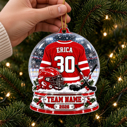 Acrylic snow globe ornament with red hockey jersey, helmet, crossed sticks, puck, holly and a silver name plaque.