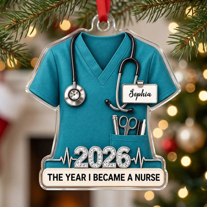 Teal scrub top acrylic ornament with stethoscope, ID badge, pocket tools, EKG line, 2026 numerals and a white name banne