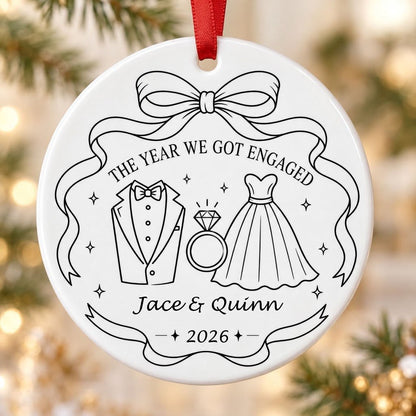 Round white ceramic ornament with black line art of bow, tuxedo, ring, dress, and THE YEAR WE GOT ENGAGED banner.