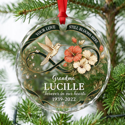 Round glass ornament with hummingbird, hibiscus, green infinity ribbon, and 'Your Love Still Blooms Here' text.