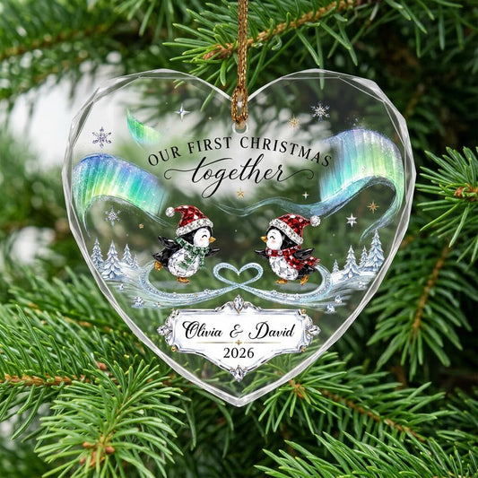 Heart glass ornament with two ice-skating penguins under green and blue aurora with names and date.