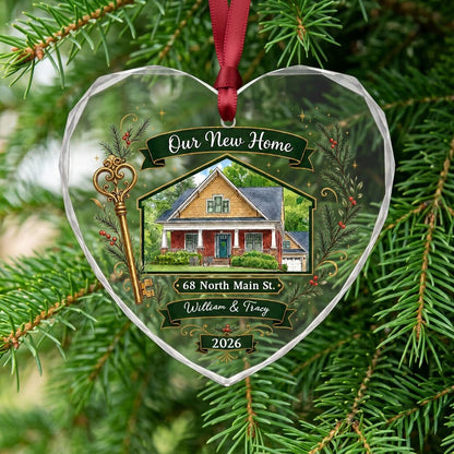 Heart-shaped glass ornament with watercolor house, gold key, evergreens, green banners, and 'Our New Home' text.