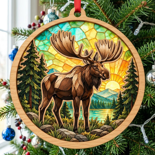 Round wood ornament with a moose, pine trees, rocks, a lake, mountains, and a glowing sun under a stained-glass sky.