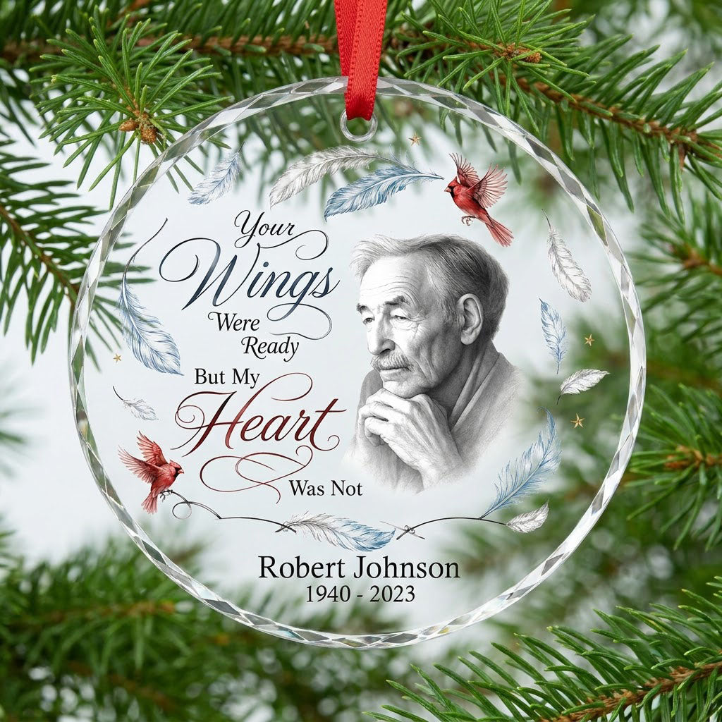 Round glass ornament with sketch portrait, two red cardinals, blue and brown feathers, and memorial name and years.