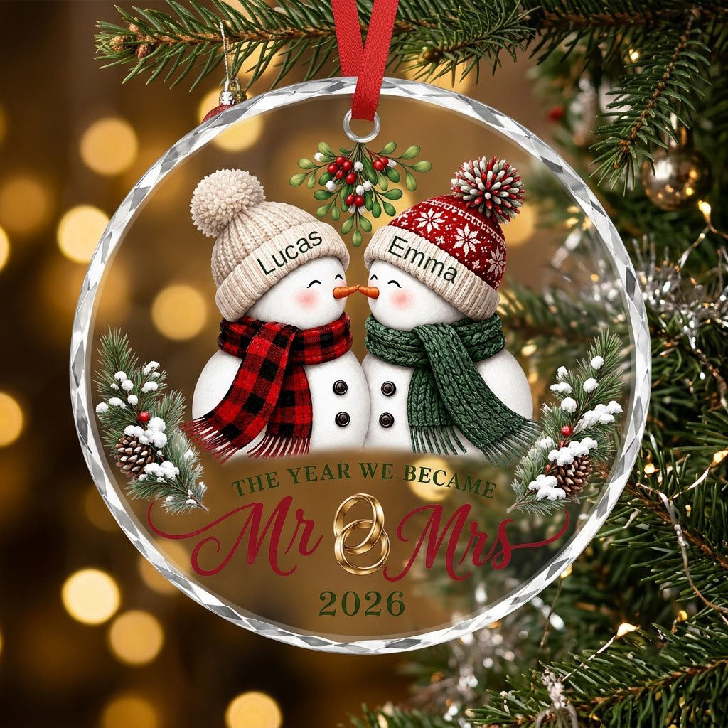 Round faceted glass ornament with two kissing snowmen under mistletoe and gold rings, personalized with names.