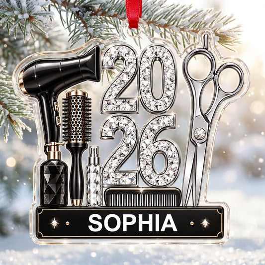 Acrylic ornament shaped around salon tools with 2026 in rhinestones and a black nameplate for a stylist's name.