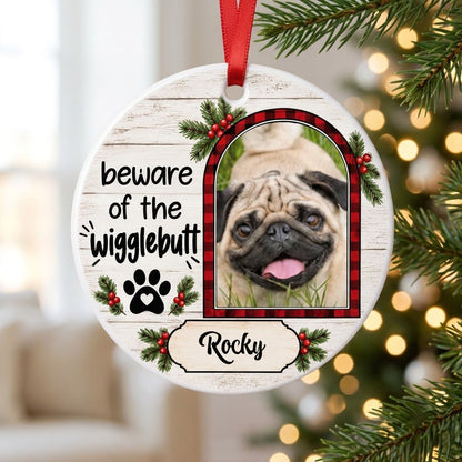 Round ceramic ornament with buffalo plaid photo frame, paw-heart, pine sprigs, and 'beware of the Wigglebutt'.