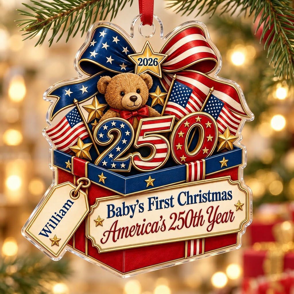 A teddy bear in a red gift box with blue trim, 250 and 2026 with American flags and a patriotic bow on an acrylic orname