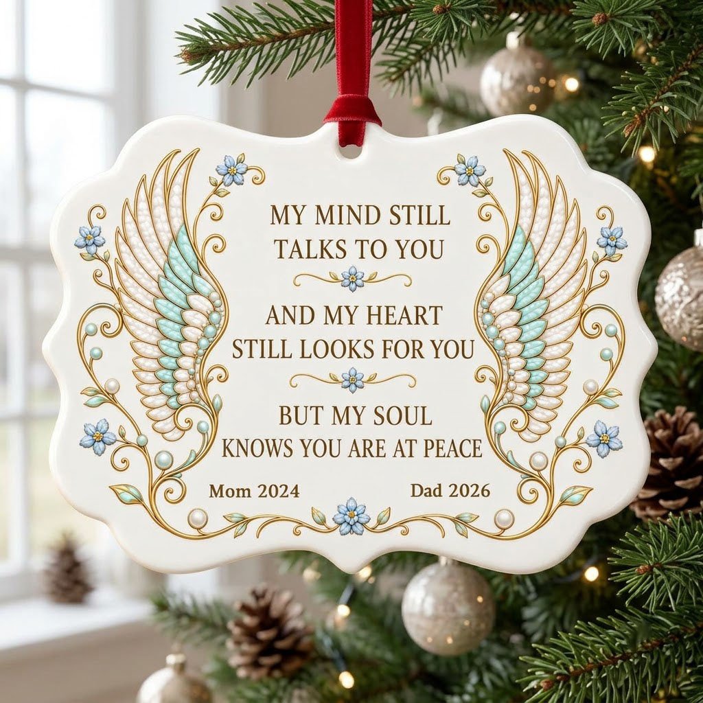Medallion ceramic ornament with gold-outlined angel wings, blue forget-me-nots, and a memorial quote with name and year.